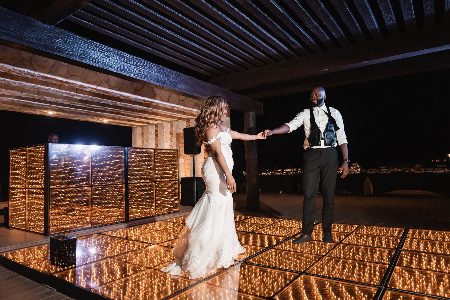 Bride and groom share first dance on glowing mirror dance floor under night sky.