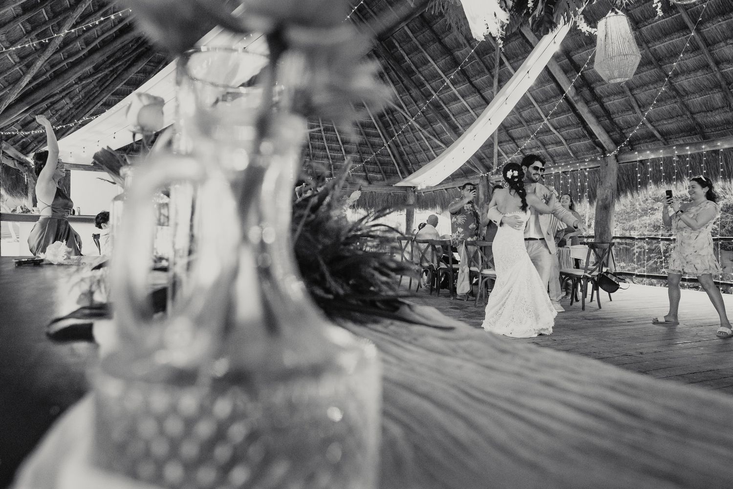 Black and white photo of bride and groom sharing first dance at tropical open-air wedding venue.