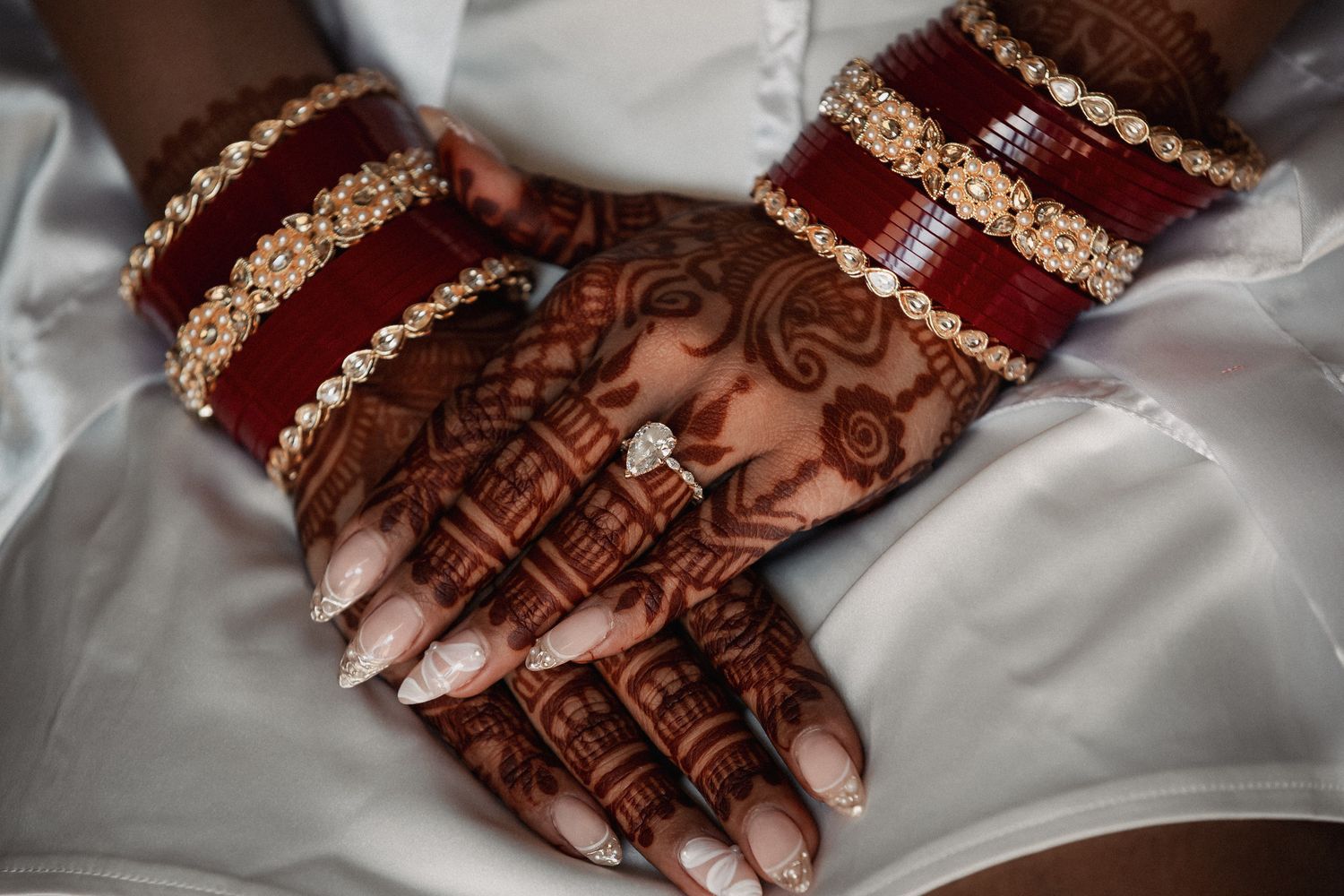 Bridal hands adorned with intricate henna mehndi design and gold red bangles with diamond engagement ring.