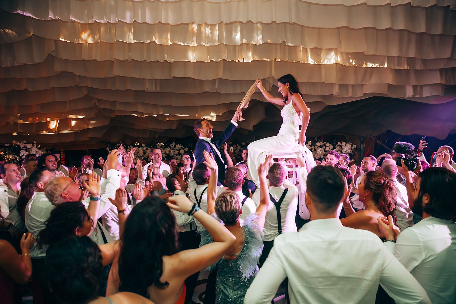 Guests dancing under elegant white draped ceiling at a wedding reception.
