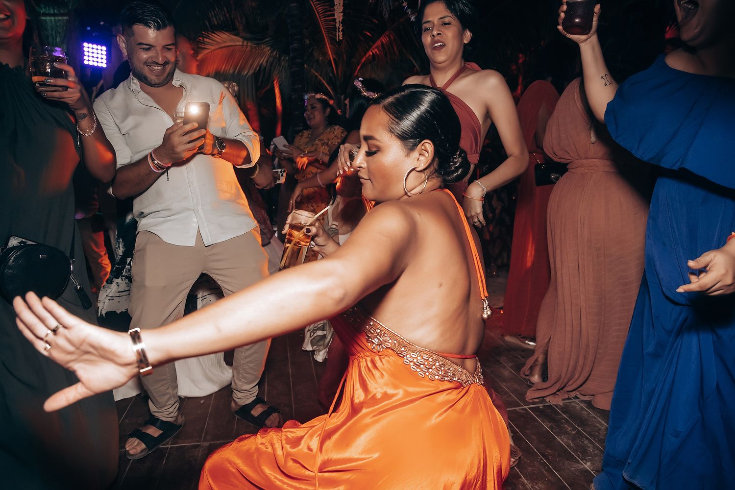 Partygoers dancing and celebrating on a crowded nightclub dance floor with vibrant lighting.