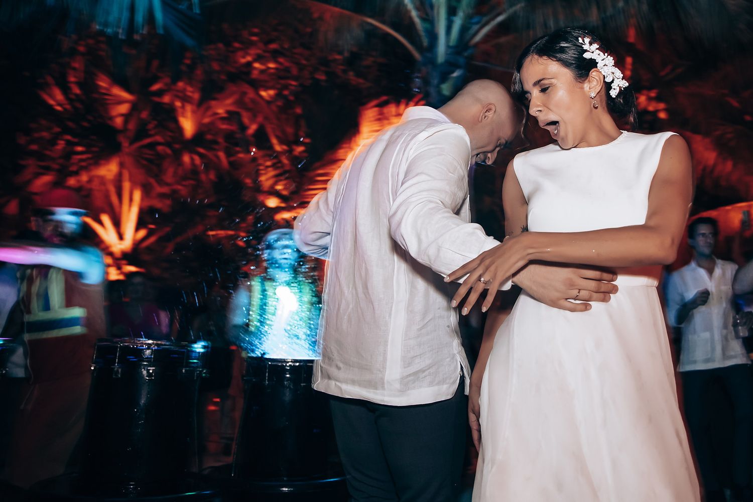 Wedding guests dancing in a dark reception venue illuminated by colorful mood lighting and disco effects.