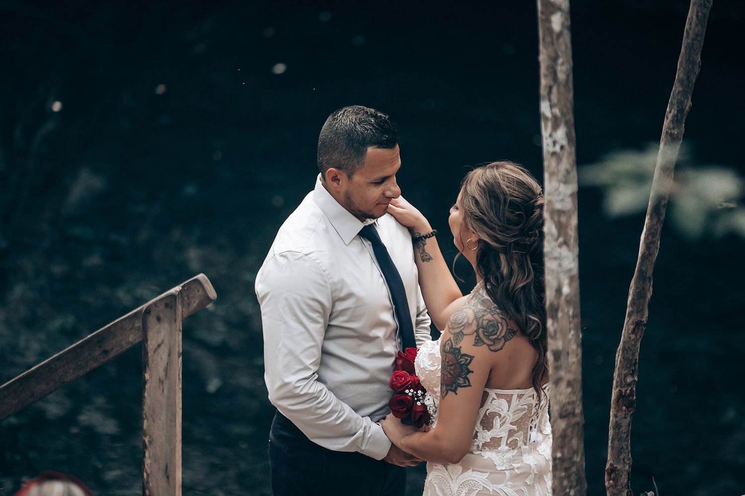 Wedding reception guests dancing and celebrating under twinkling lights in a wooded outdoor venue.