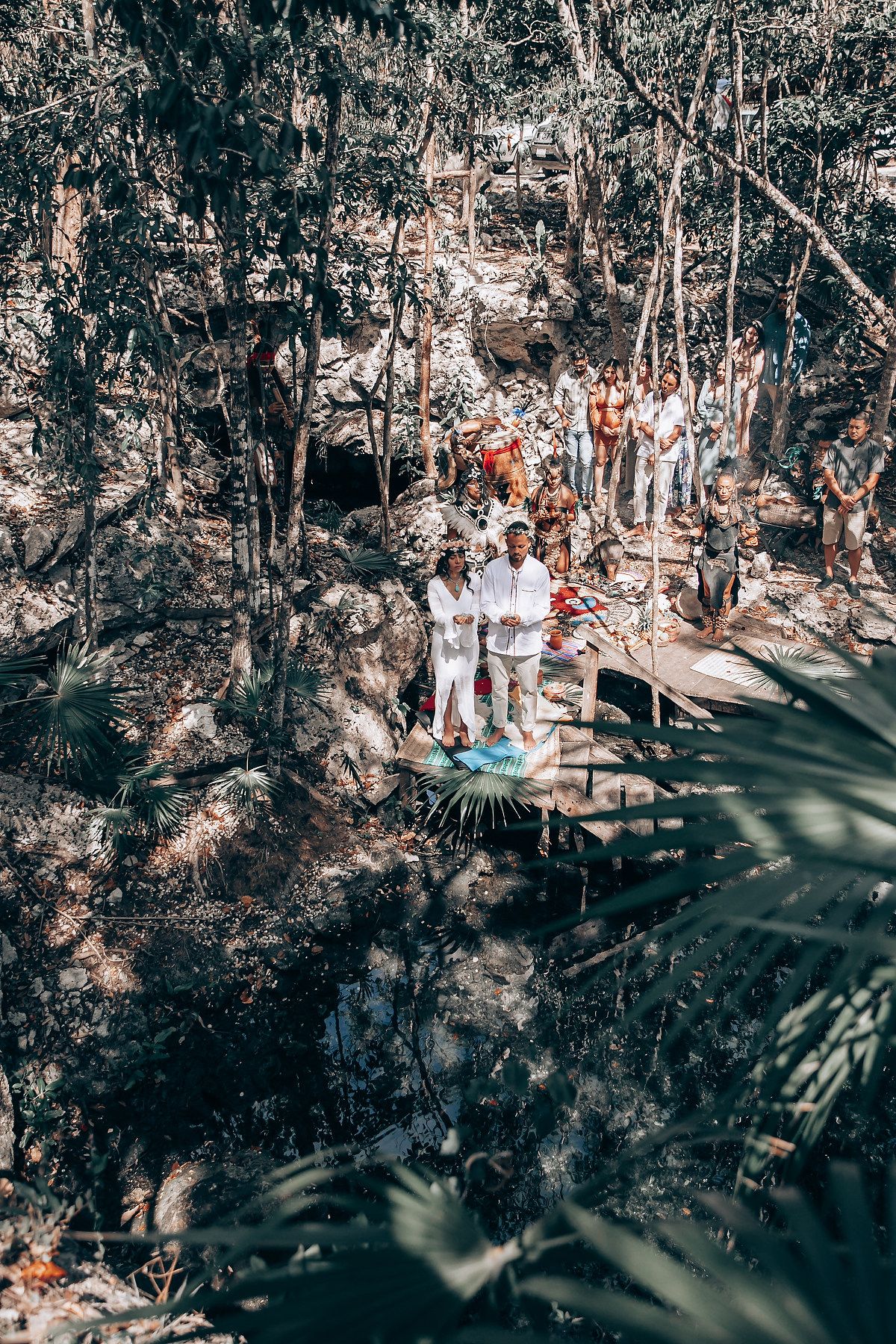 Group of people gathered in a lush forest setting wearing white clothing for a spiritual ceremony.
