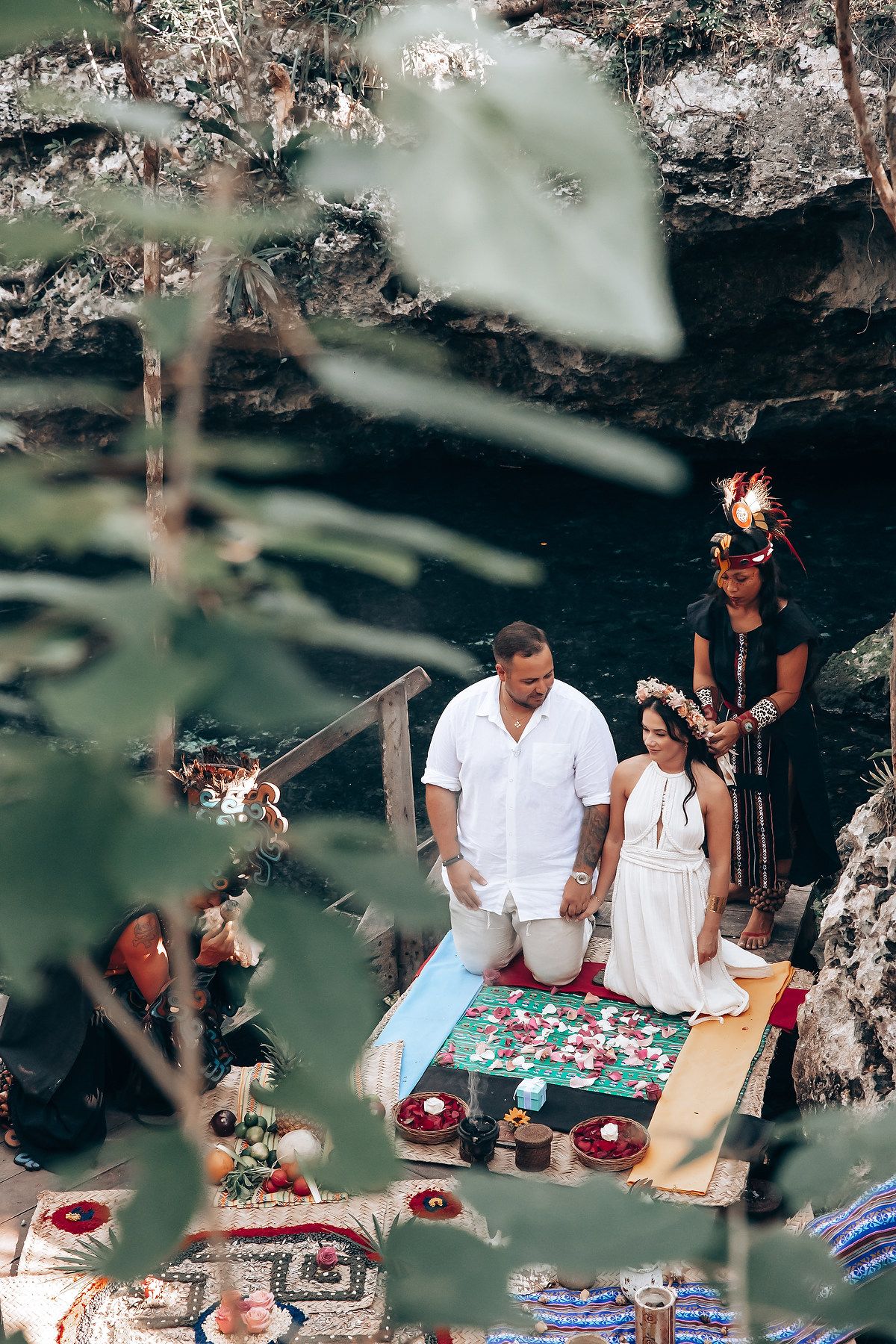 Couple participates in traditional ceremony with colorful blankets and decorative items laid out on the ground.