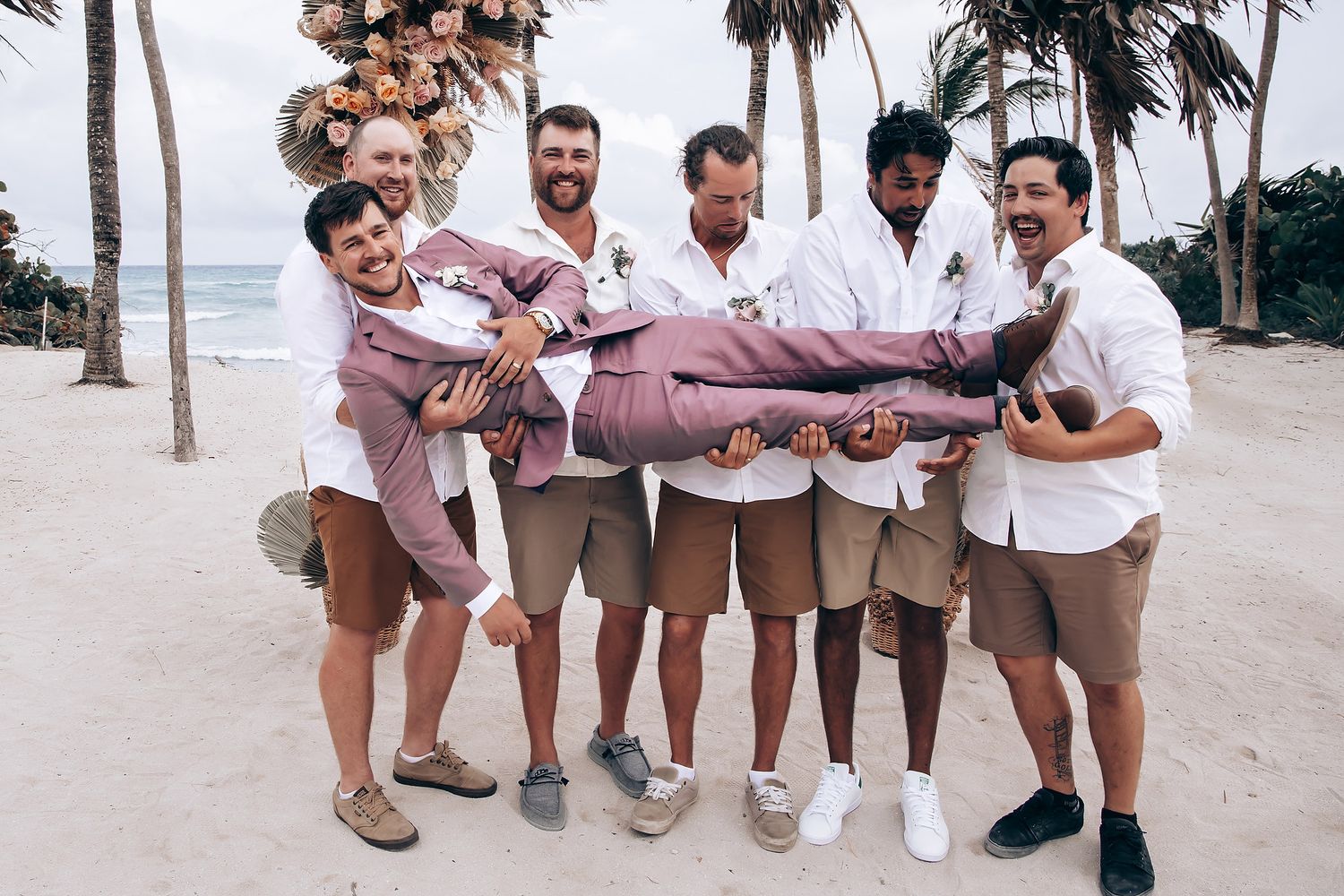 Groomsmen in light colored suits posing casually on the beach.