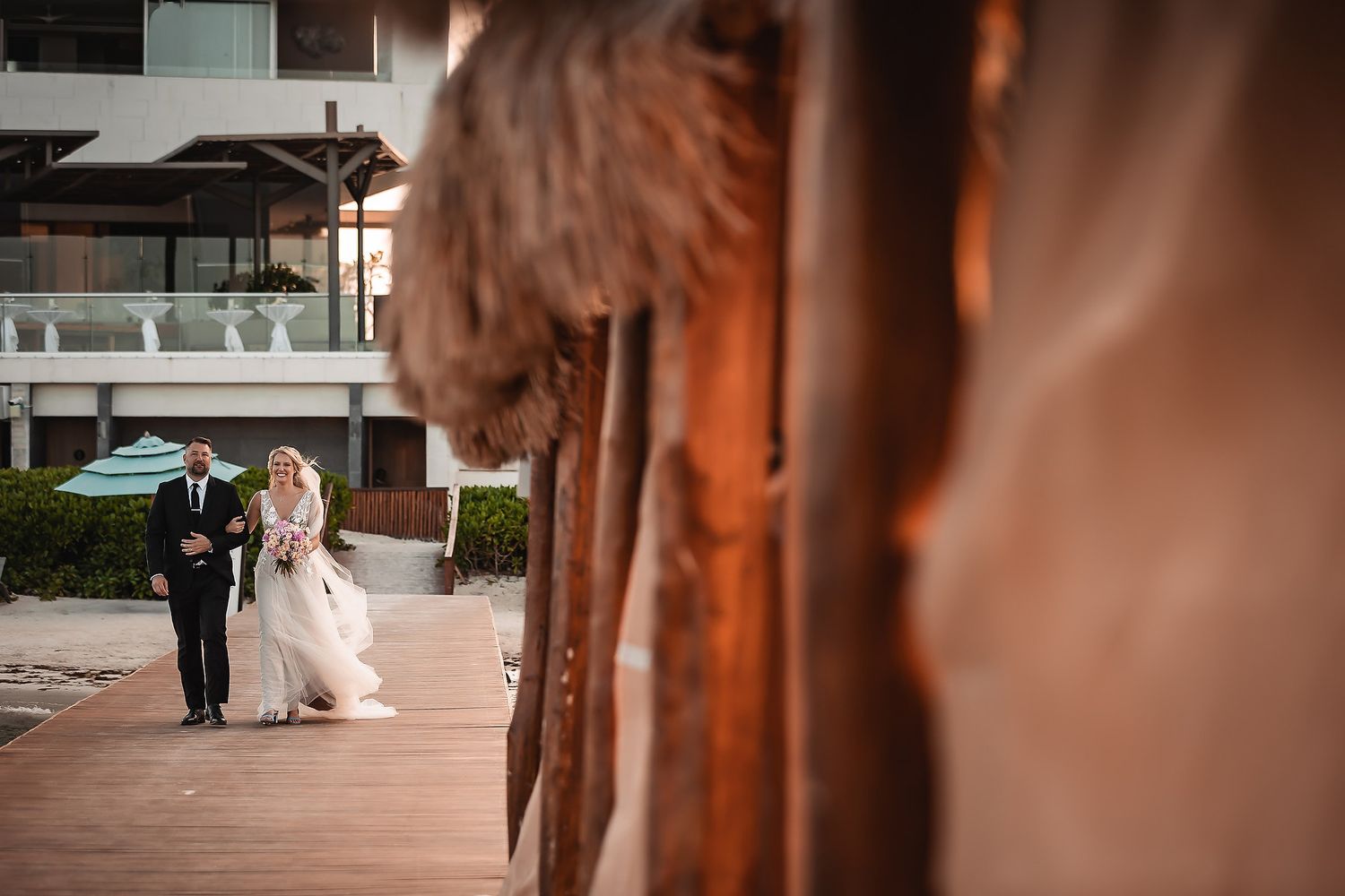 Wedding couple walking together under rustic wooden beams at beach venue.
