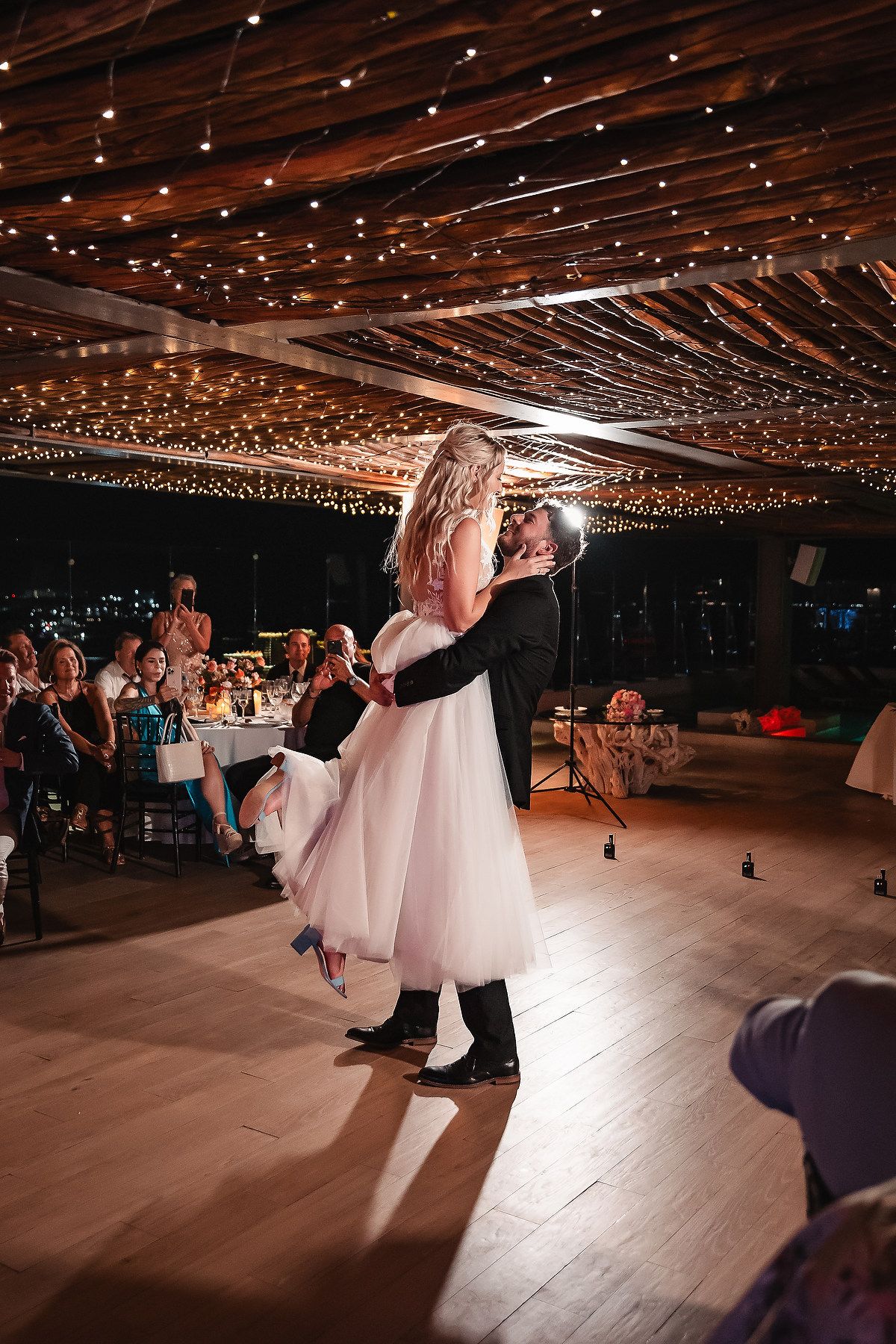 Wedding reception dance floor under twinkling string lights with couples dancing.