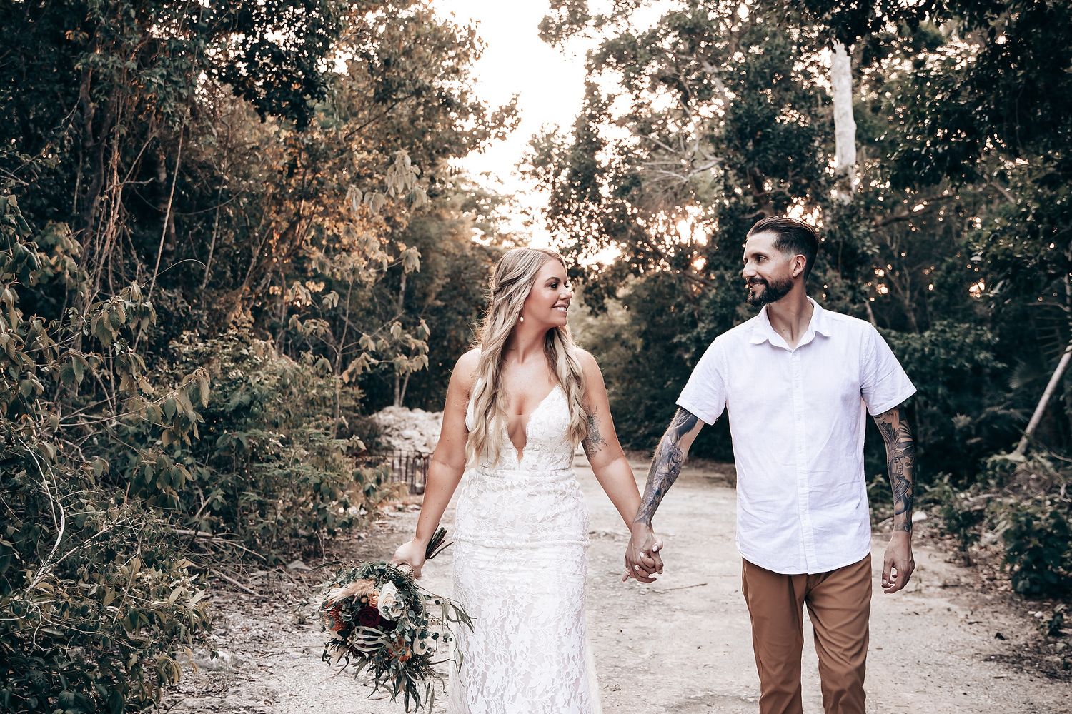 Couple walking hand in hand along a tree-lined path in natural lighting.