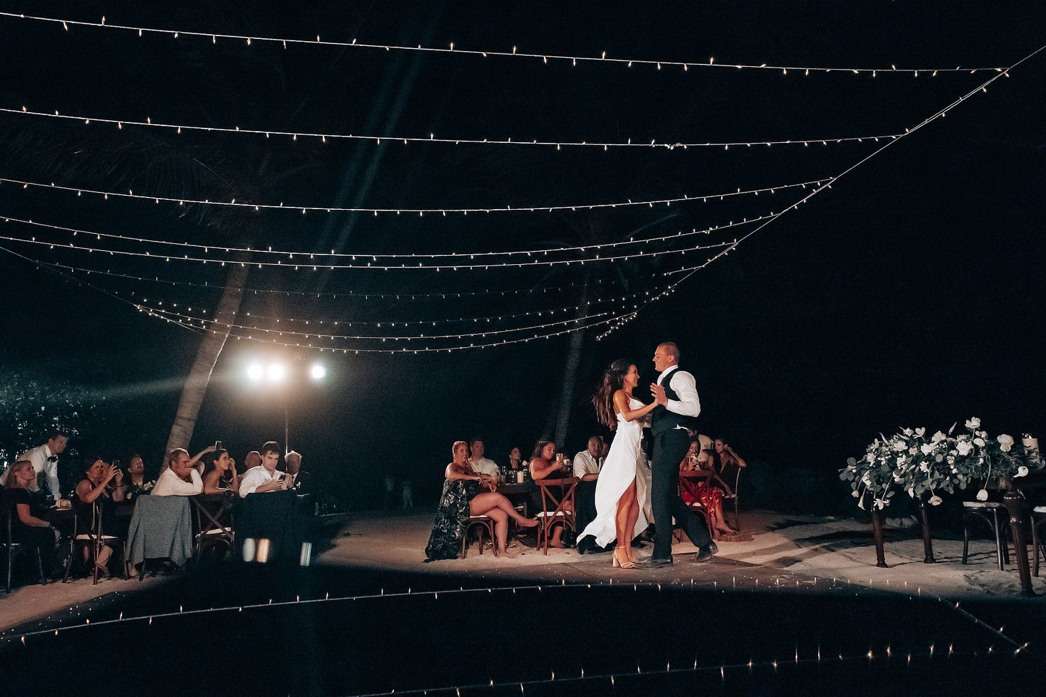 String lights illuminate an outdoor evening wedding reception space.