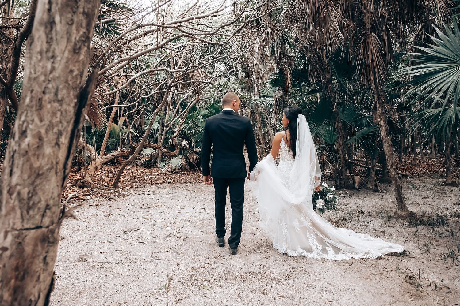 A couple walking together on a scenic outdoor path surrounded by lush tropical foliage and trees.