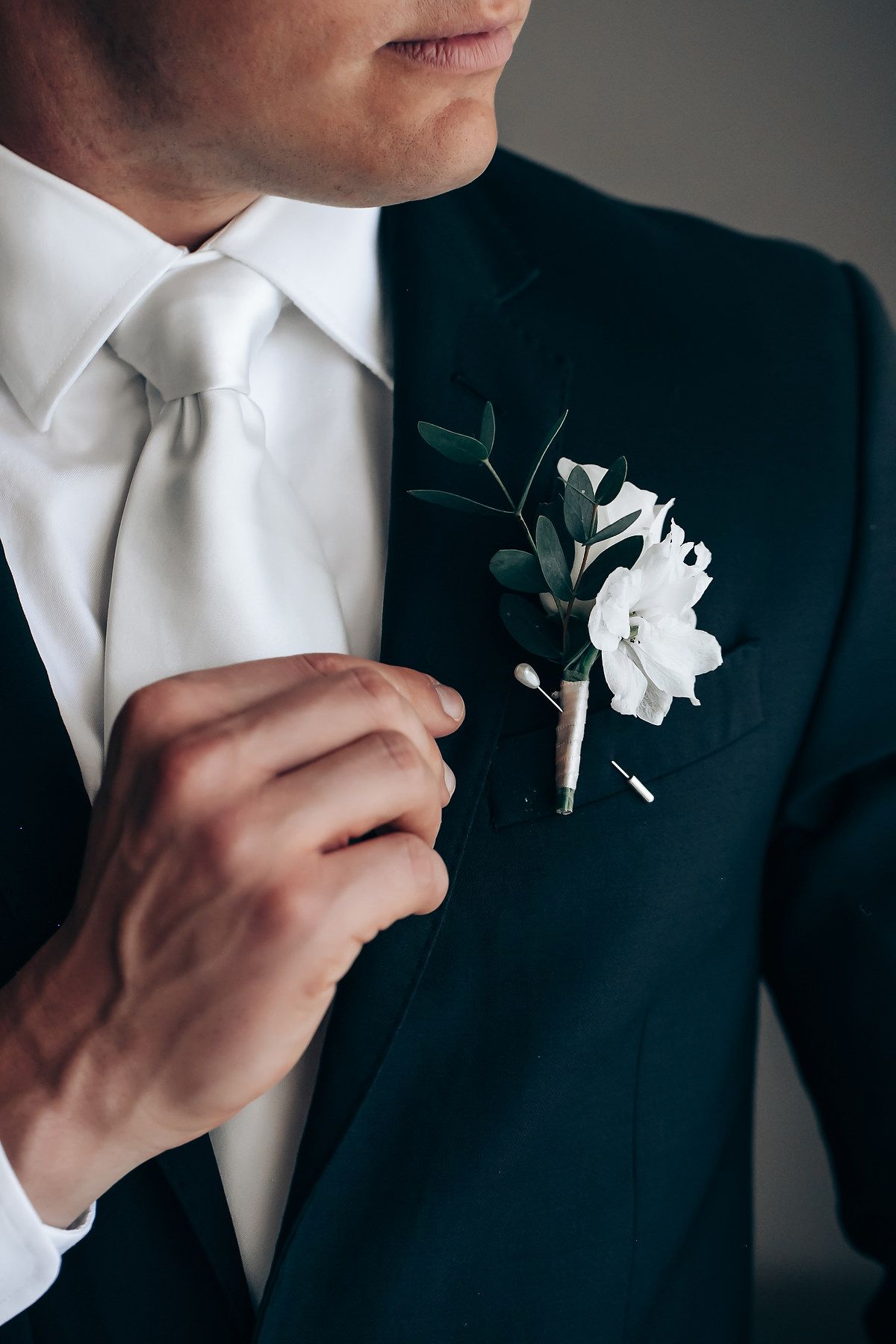 Groom adjusting white boutonniere flower on black suit jacket lapel.