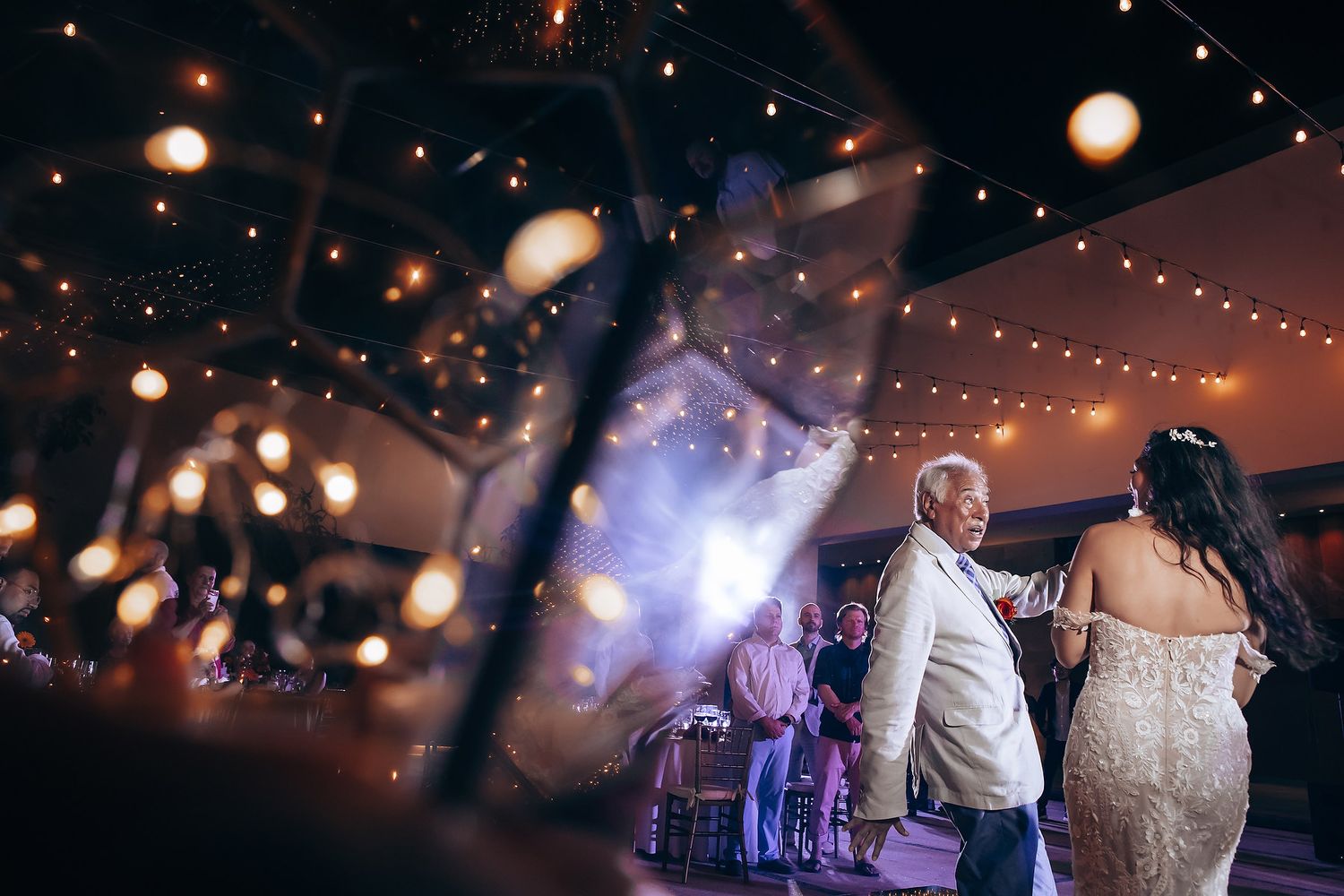 Wedding reception dance floor illuminated with string lights and purple ambient lighting.