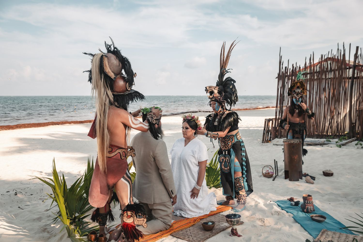 Couple exchanges vows in a traditional Mayan beach ceremony with costumed officiants in elaborate headdresses.
