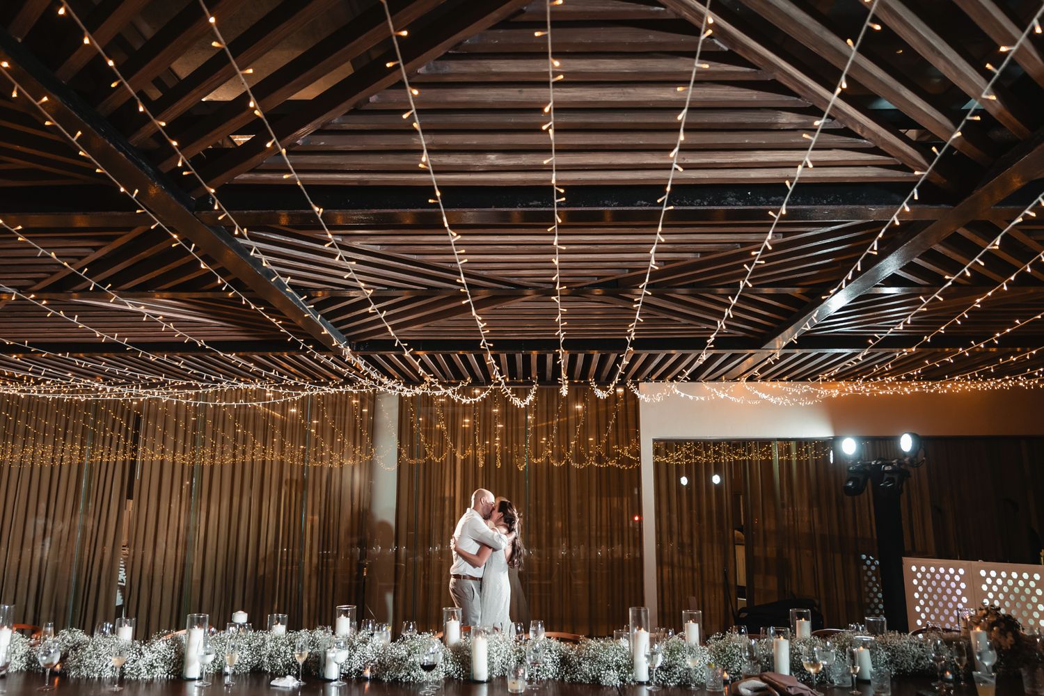 Couple shares first dance under twinkling fairy lights in elegant rustic wedding reception venue.