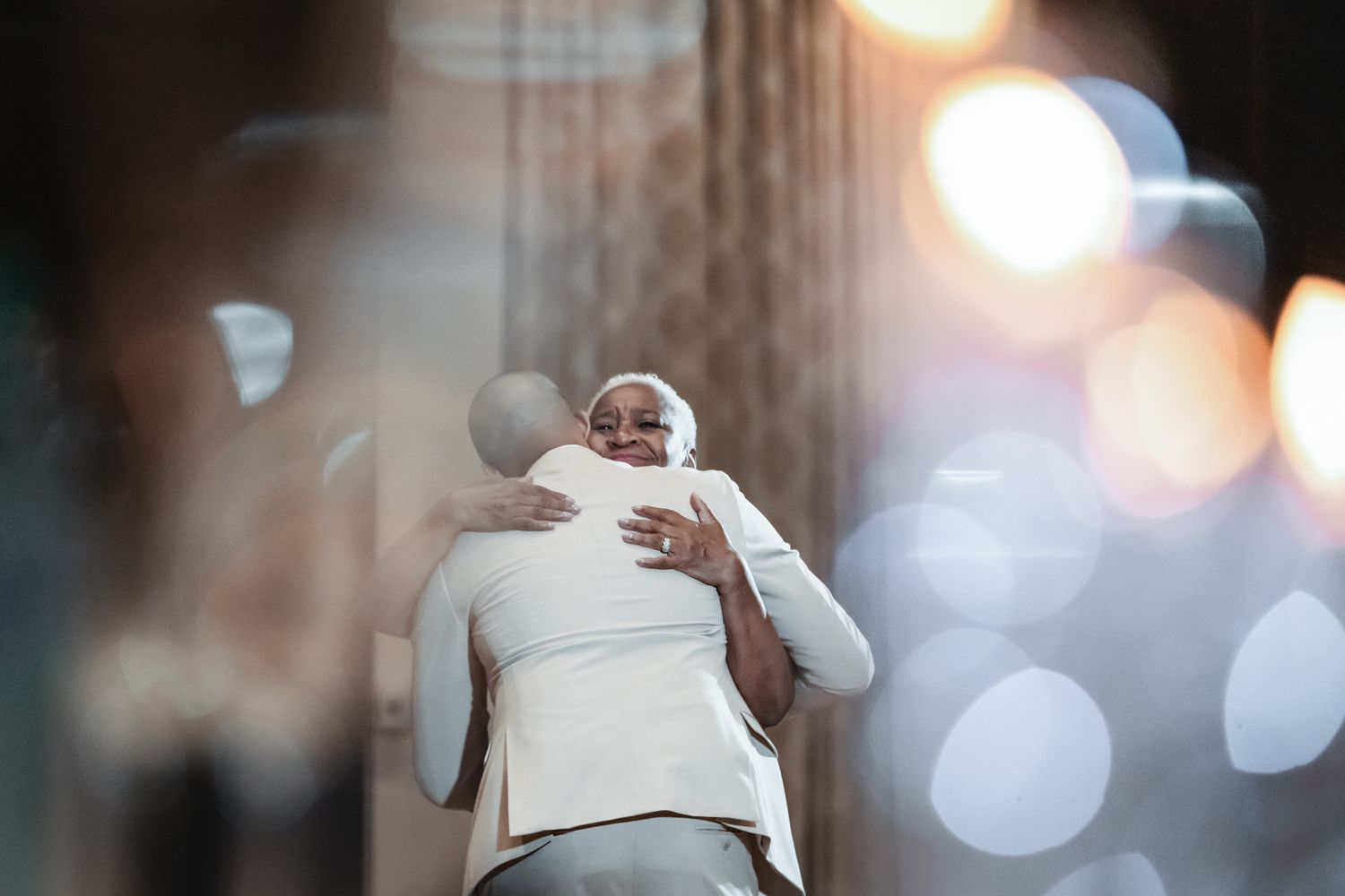 Two people sharing a warm embrace, with soft bokeh lights in the background creating an emotional moment.
