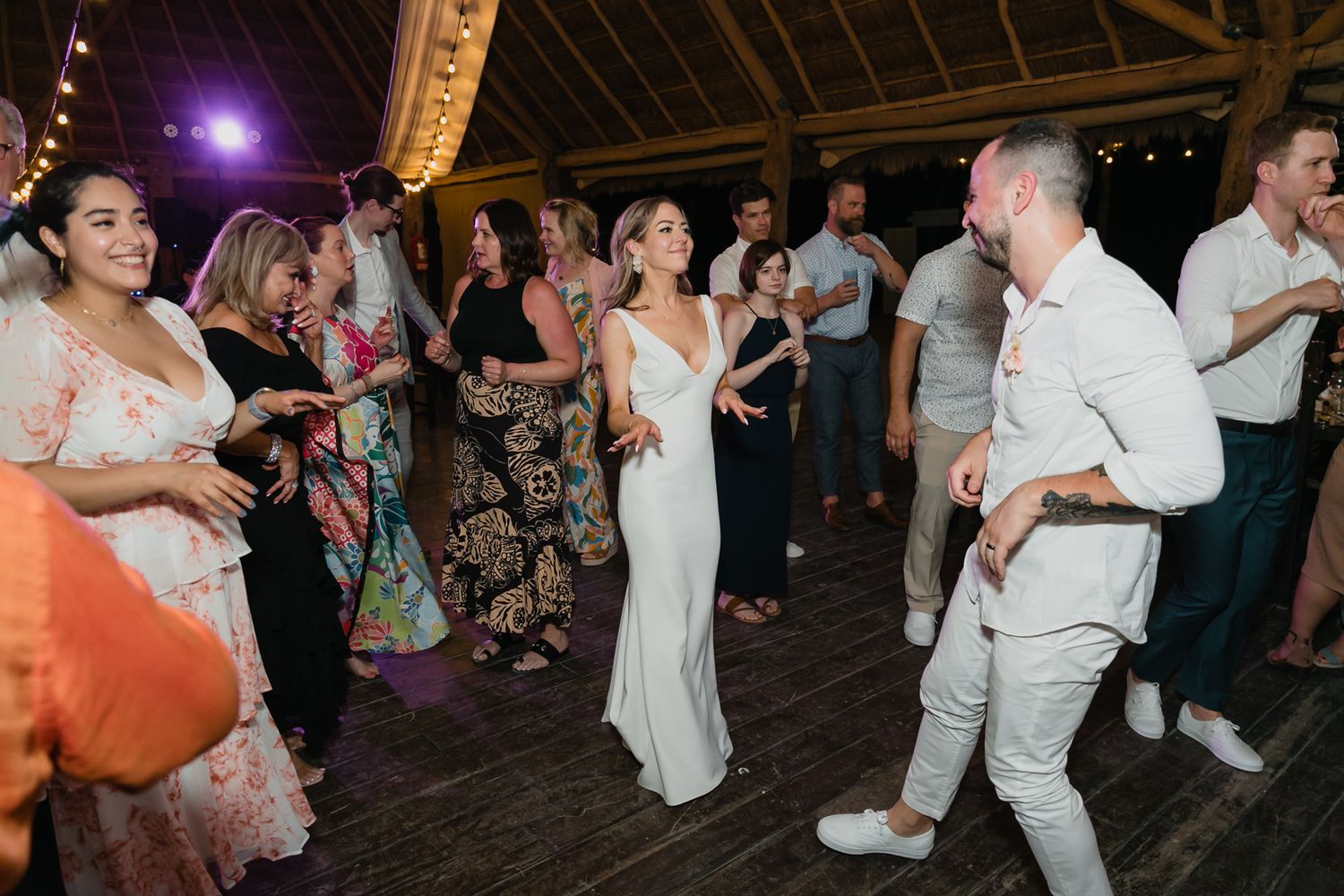 Bride and groom dance energetically with guests at a colorful tropical wedding reception.