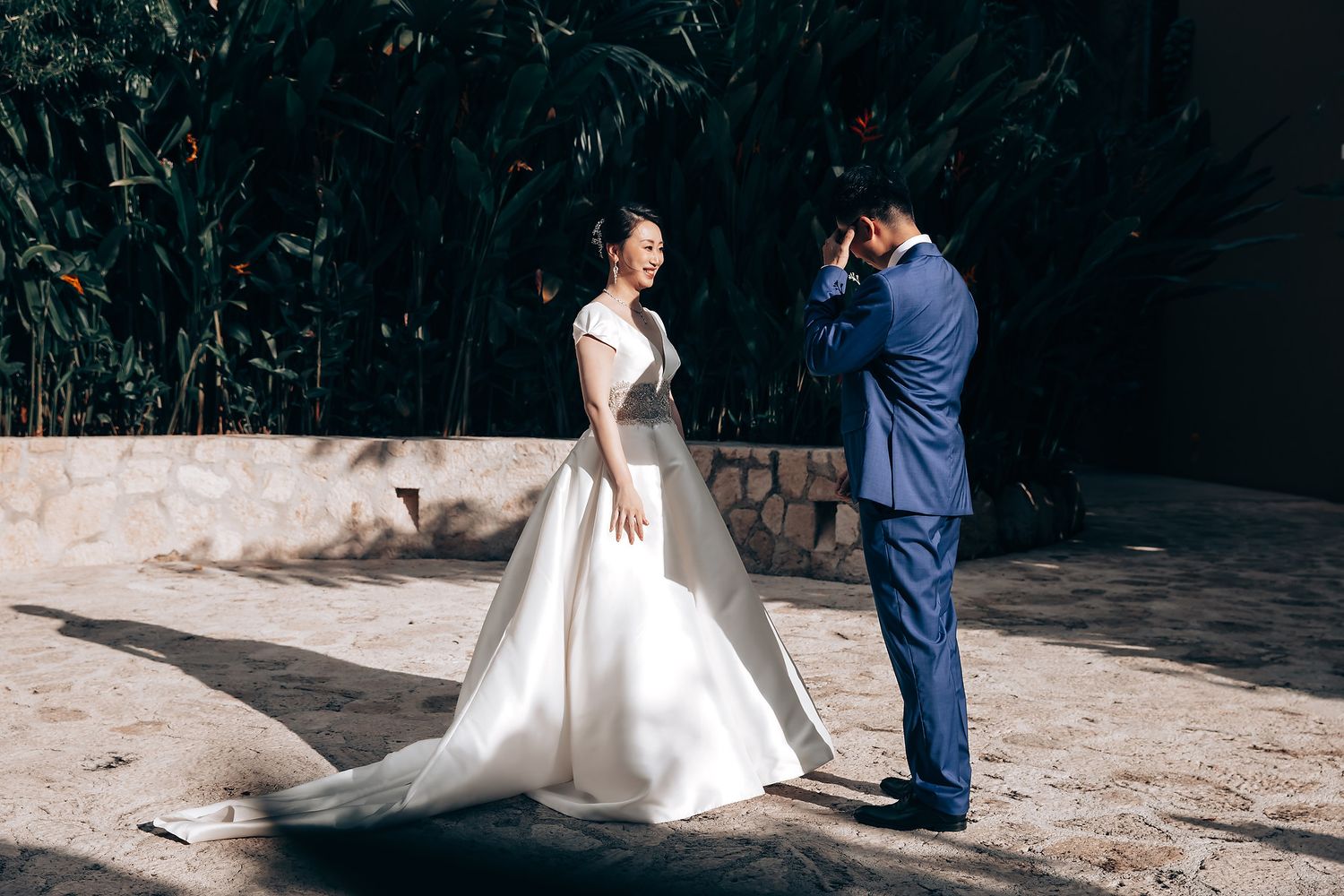 Couple in wedding attire standing in outdoor setting with natural backdrop.