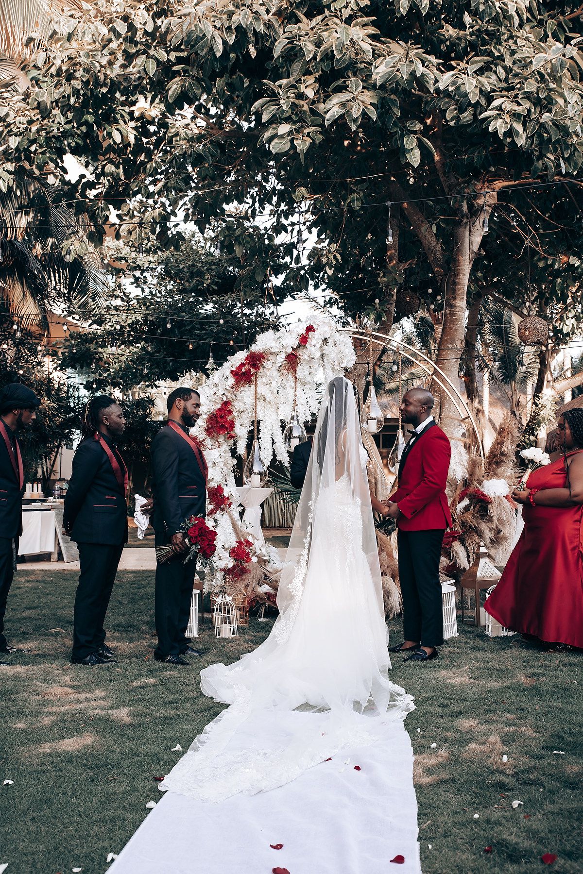 Outdoor wedding celebration under trees with flowing white dress and burgundy accents.