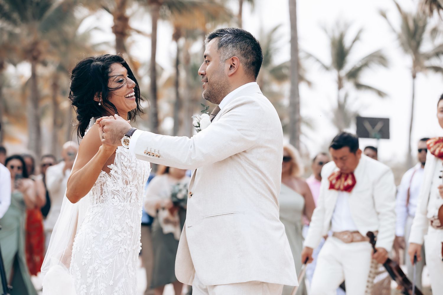 A couple dances joyfully on the beach during their tropical wedding celebration.