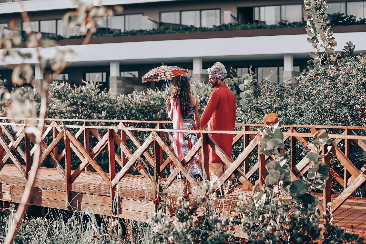 Wooden boardwalk with railing surrounded by lush greenery and architectural elements.