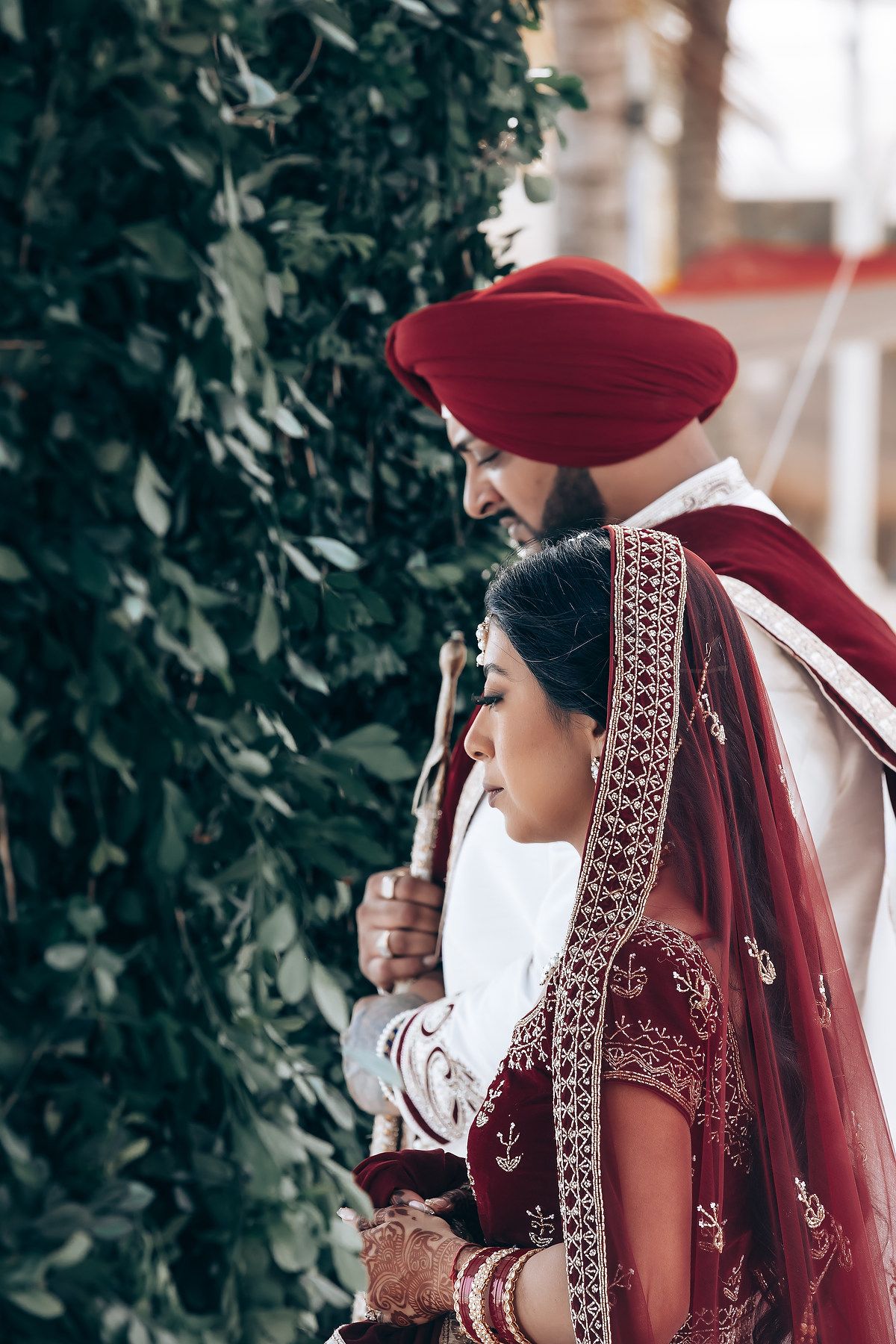 Bride in deep red traditional Indian wedding attire with intricate embroidery and veil details.