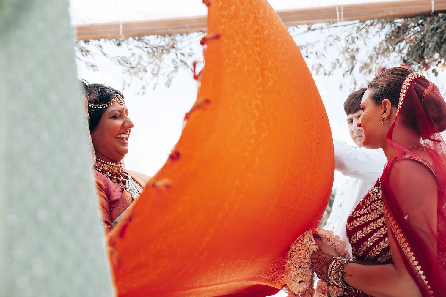 Wedding guests in vibrant orange and red traditional attire gathered for a beach ceremony.