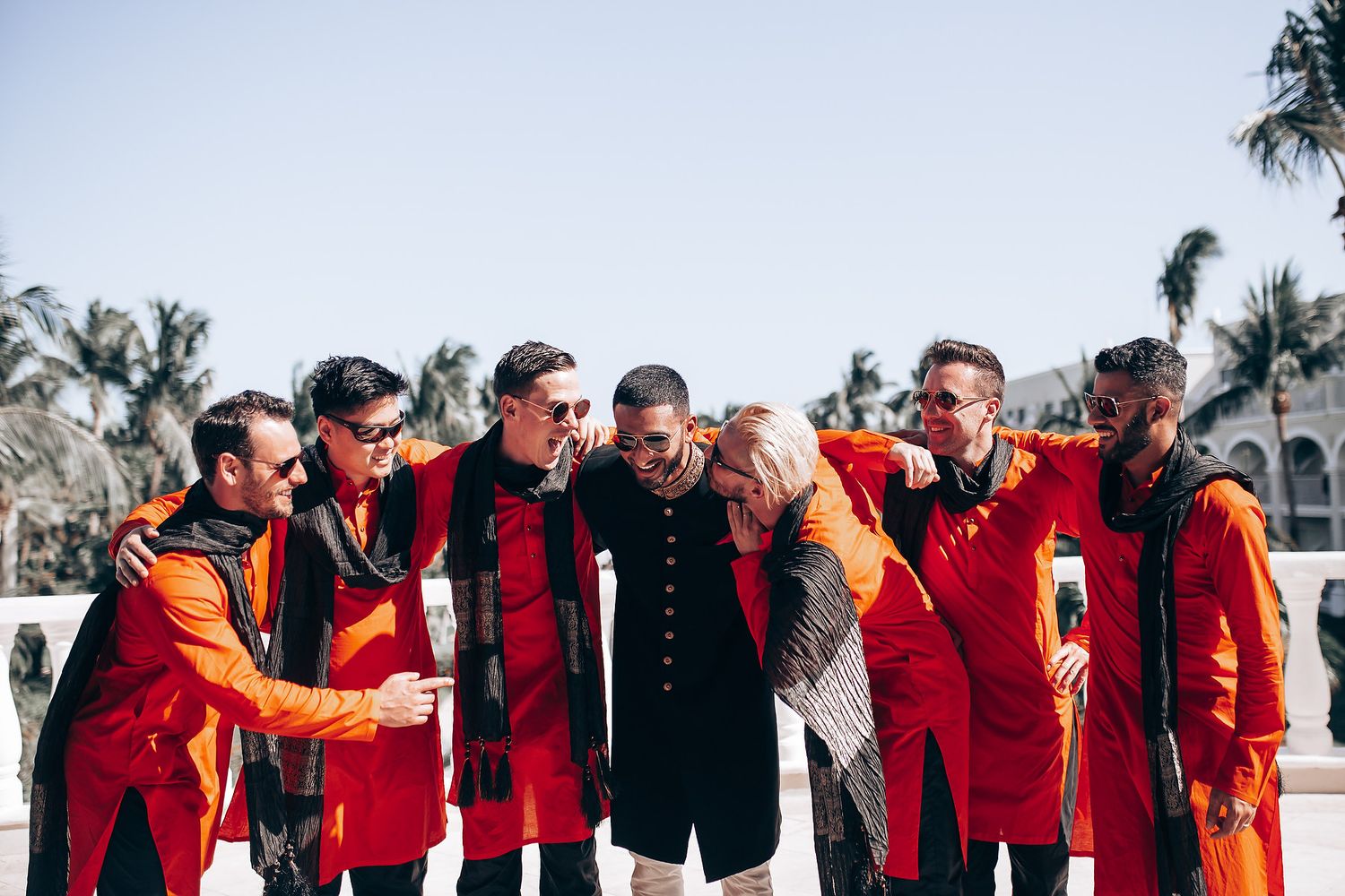 Groomsmen in matching red jackets pose together outdoors in a fun celebratory moment.