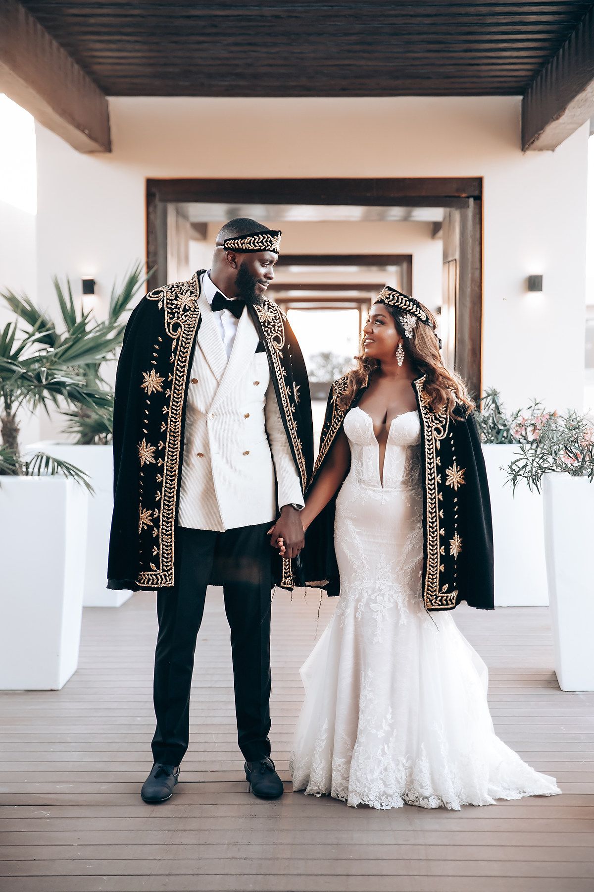 Wedding couple in formal attire poses in an elegant hallway with white columns and wooden details.