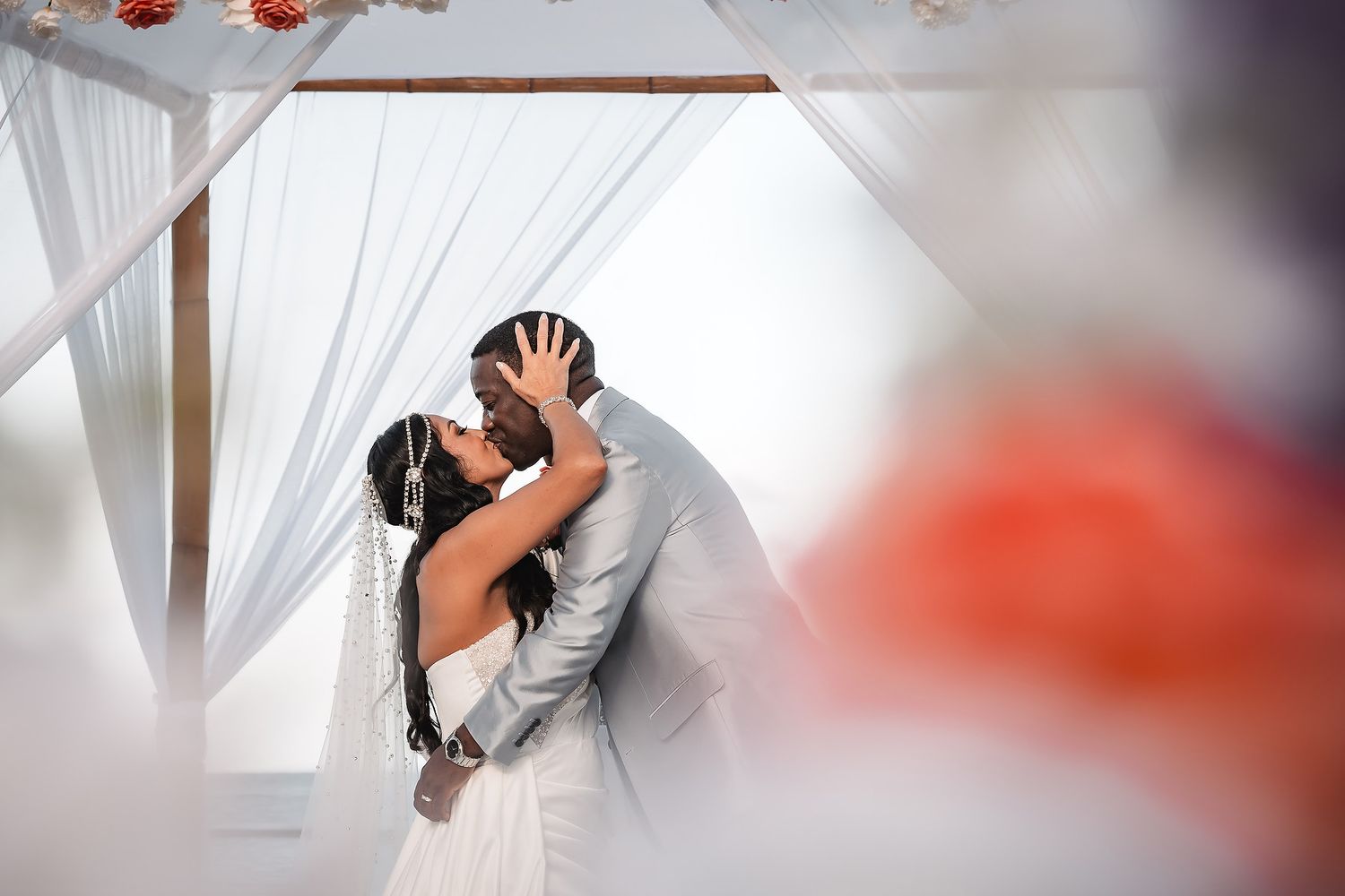 Wedding celebration under white fabric draping with coral floral decorations.