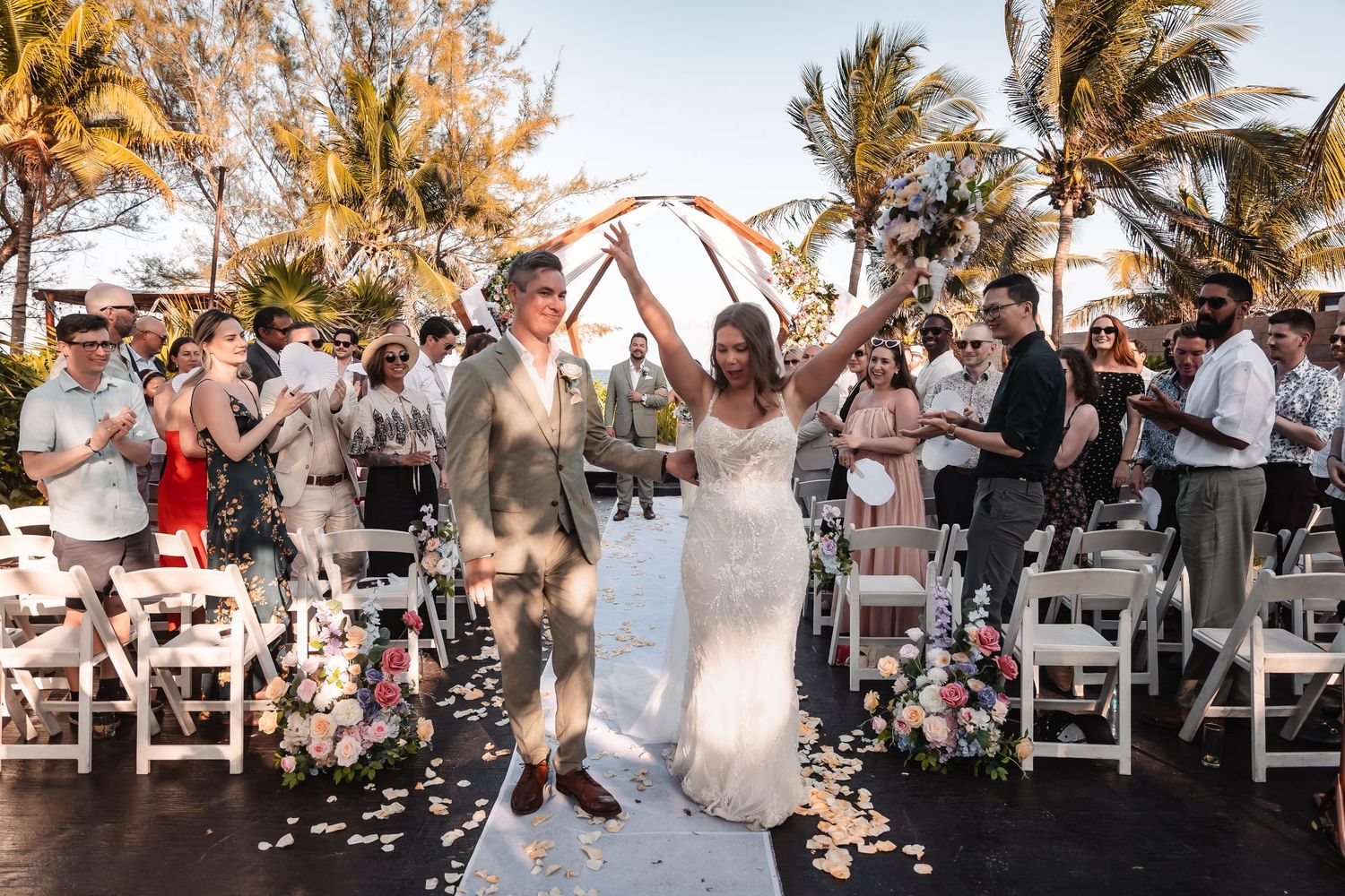 Festive outdoor wedding celebration with guests gathered under palm trees.