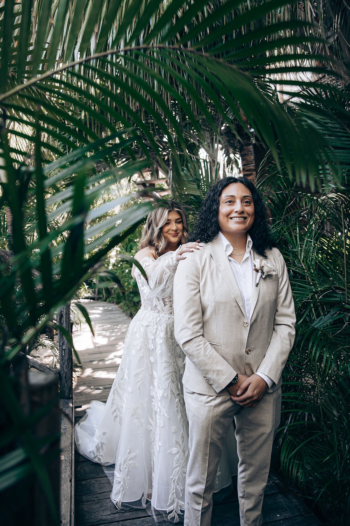 A romantic wedding photo series showing a couple in white and beige outfits posing among tropical palm fronds.
