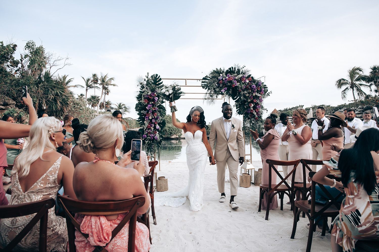 Beachfront wedding ceremony with guests seated on wooden chairs facing the ocean.