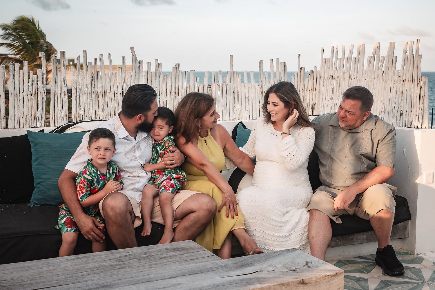 Friends gathered on a beachfront wall during golden hour with palm trees in the background.