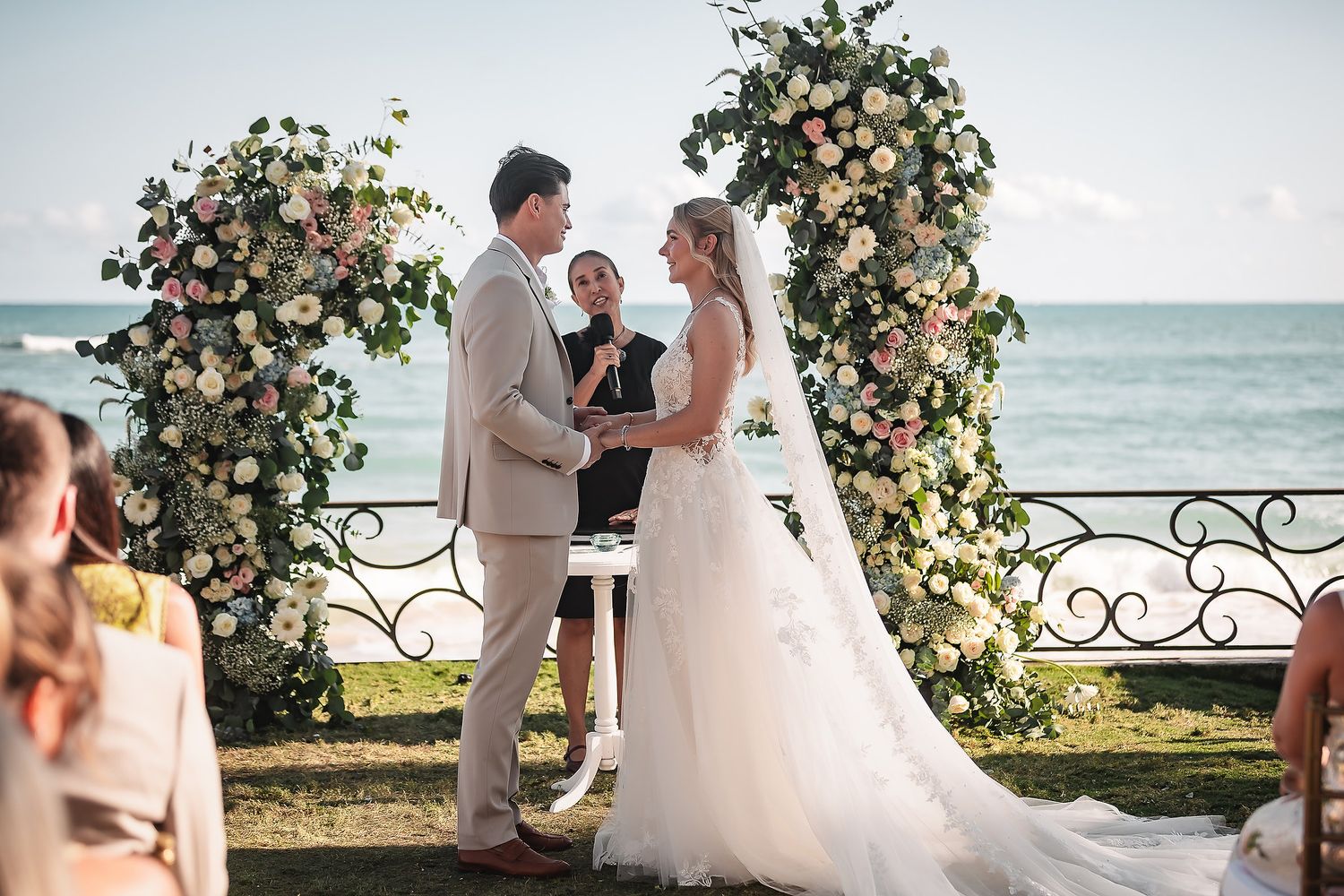 Wedding ceremony arch decorated with peach and white flowers against an ocean backdrop.