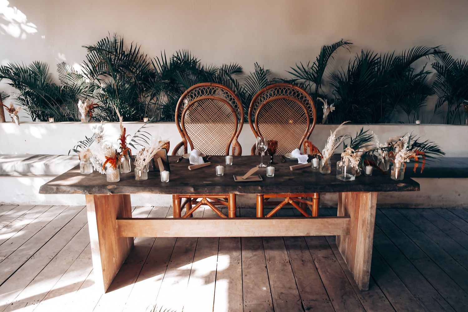 A rustic wooden bench with woven rattan chairs sits on a sunlit deck overlooking a scenic outdoor view.