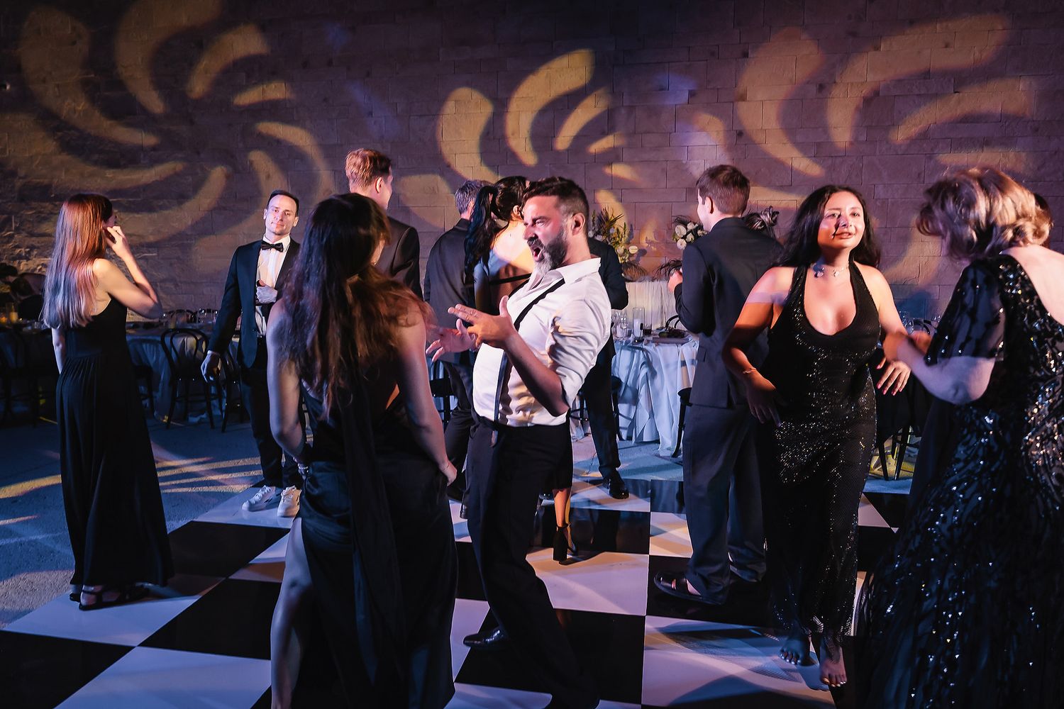 Wedding guests dancing on illuminated dance floor with purple ambient lighting and decorative patterns.