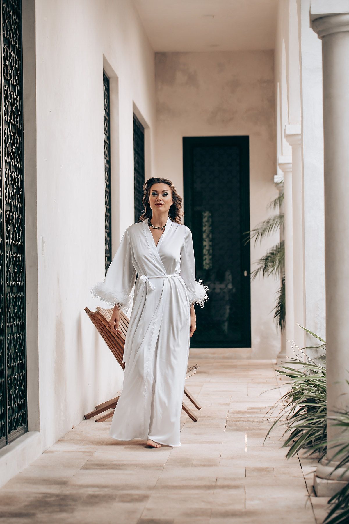 A figure in a white robe stands in an elegant corridor with arched doorways and ornate iron gates.