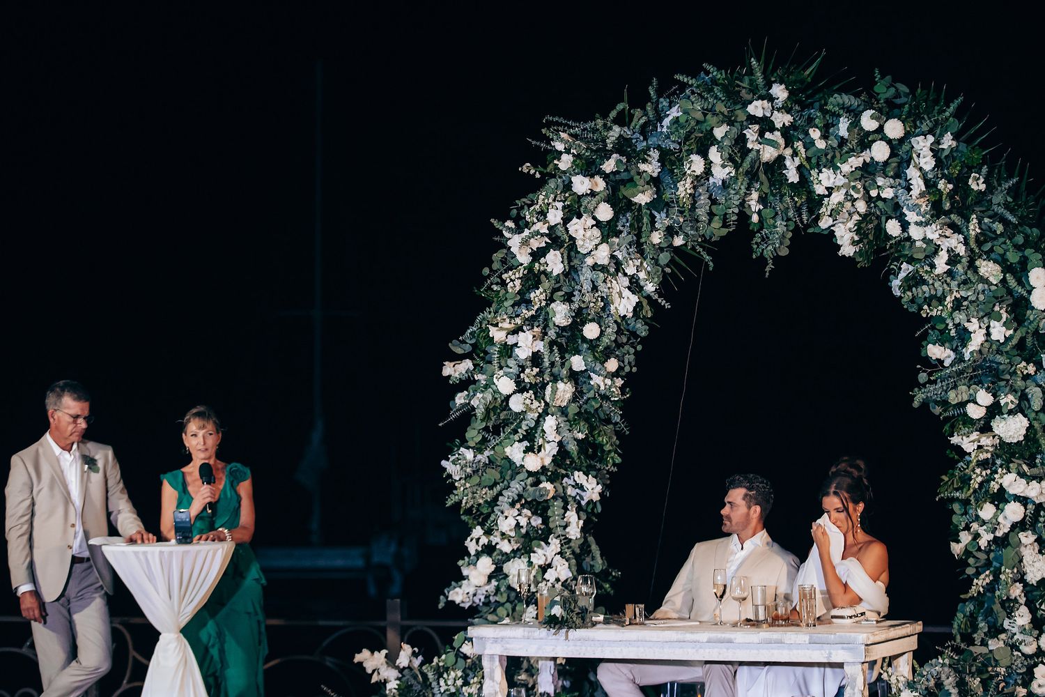 A wedding celebration under floral arches with elegant decor and romantic lighting at an evening reception.