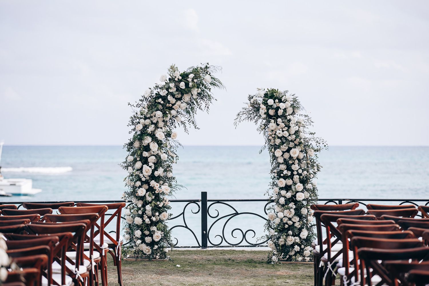 Wooden benches decorated with floral arrangements overlook a scenic ocean view at a coastal wedding ceremony setup.