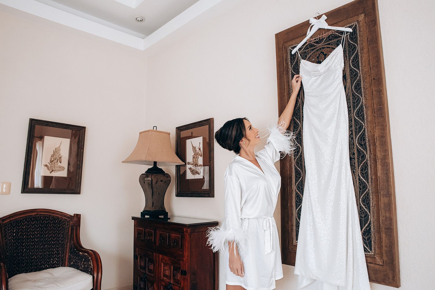 A row of elegant white wedding dresses hanging on wooden hangers against a cream-colored wall.