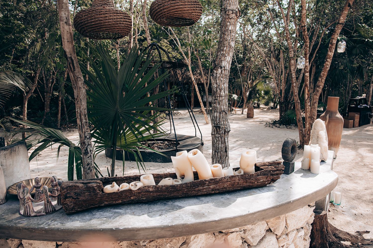 A curved white concrete bench follows a winding path through a lush tropical garden setting with tall trees.