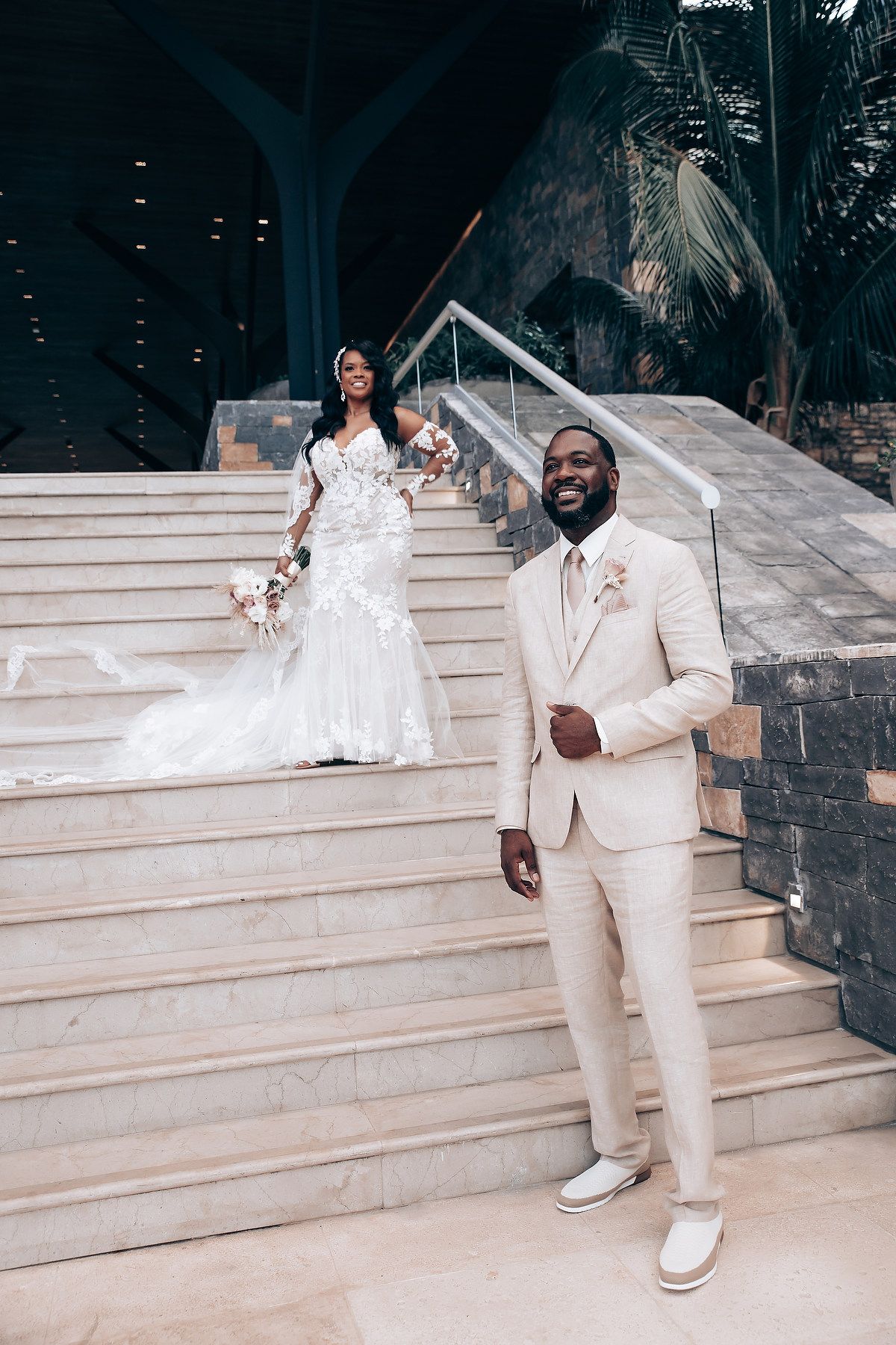 Wedding couple posing on grand white marble steps in elegant attire.