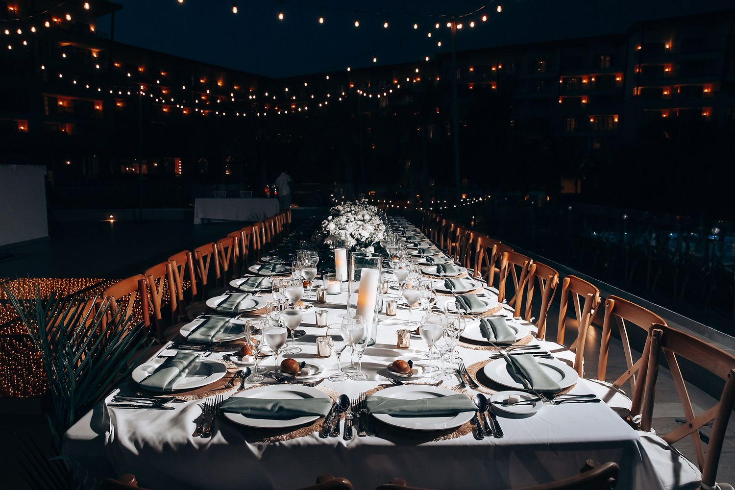 Long elegant dining table setup with string lights overhead creating a romantic ambiance.