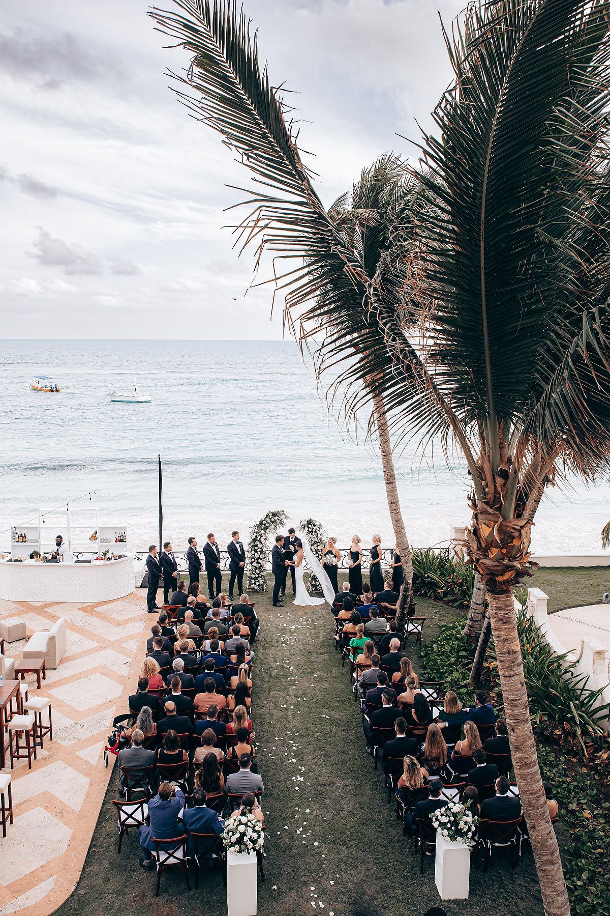 Beachside wedding ceremony setup with palm trees and white chairs arranged in rows facing the ocean.