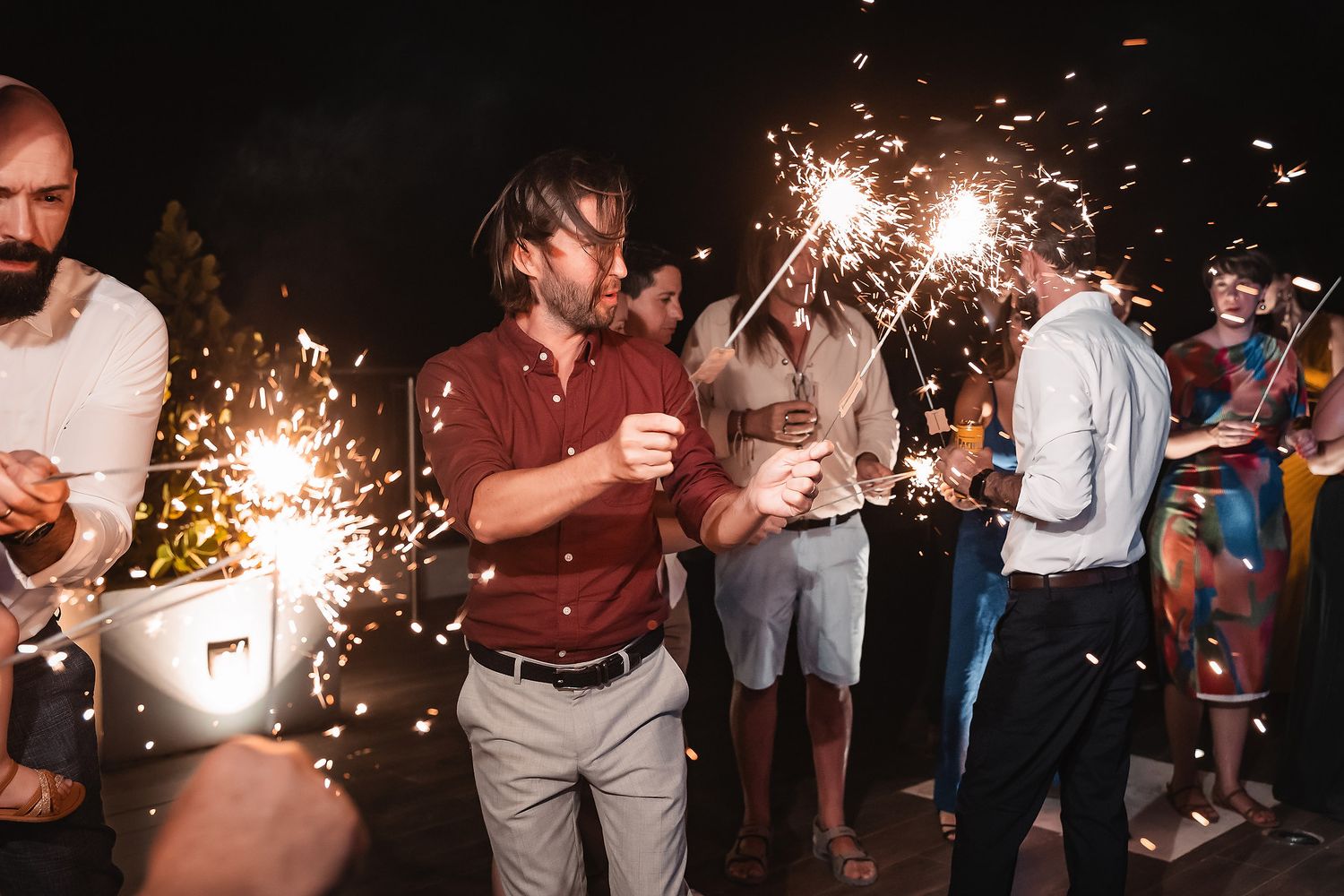 Wedding celebration with guests holding sparklers during nighttime festivities.
