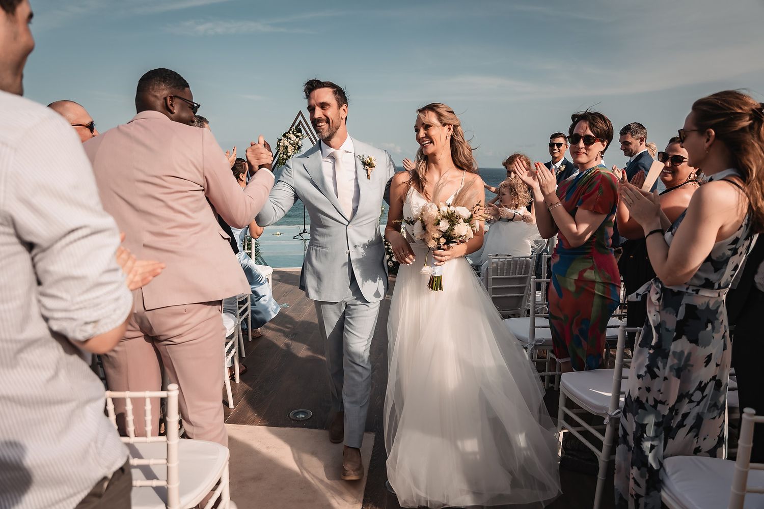 Wedding guests celebrate during an outdoor beach reception with joyful dancing and laughter.