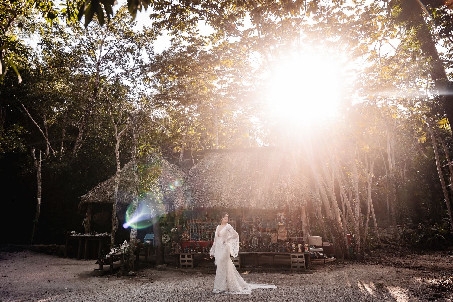 A dreamy backlit wedding photo showing a figure in white walking near a rustic structure in a forest setting.