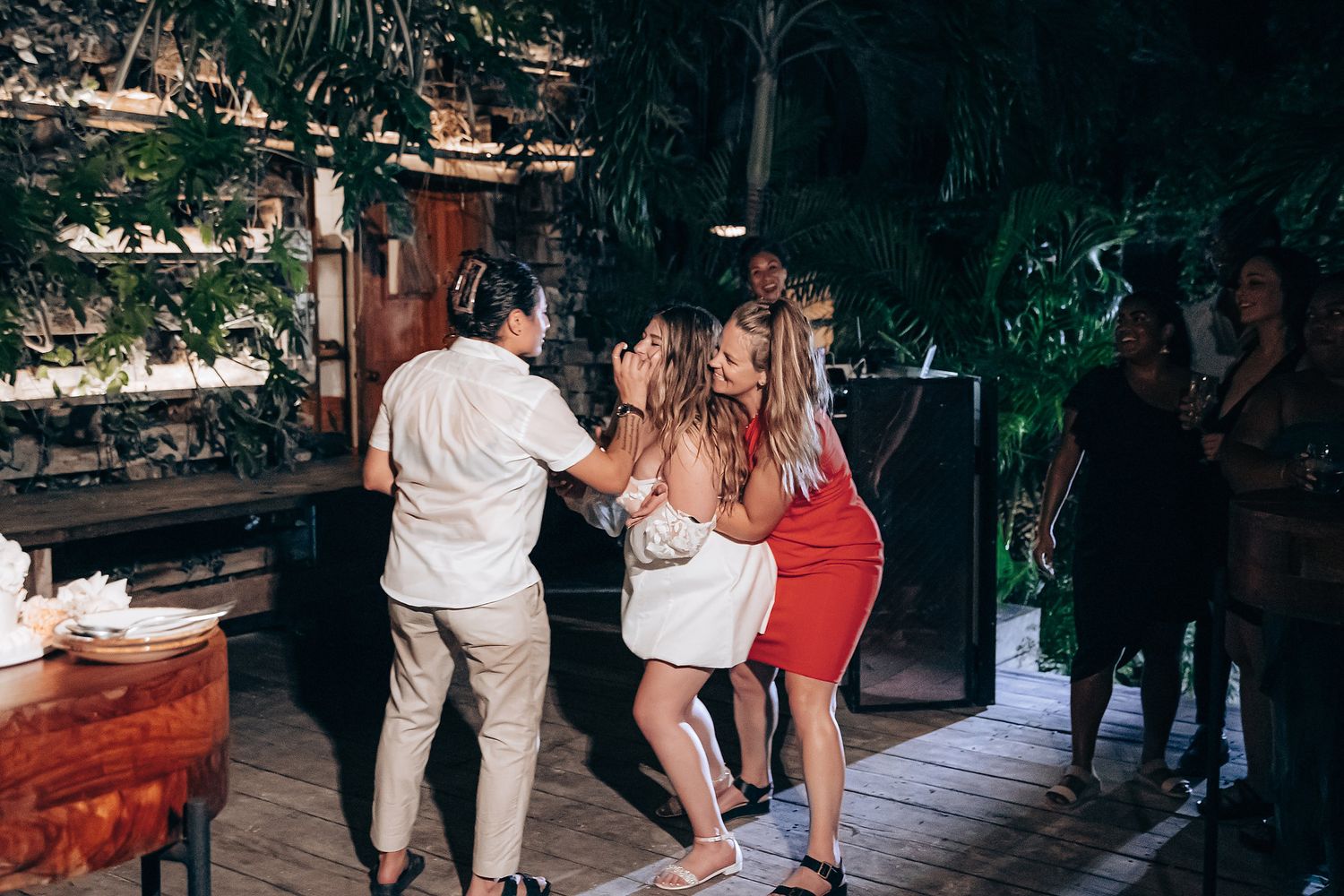 A group of people dancing and socializing at an outdoor patio party with string lights overhead.