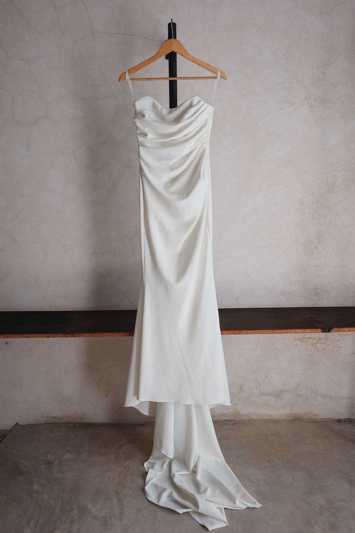 Elegant strapless white satin wedding gown with a cowl neckline and train hanging on a wooden hanger.